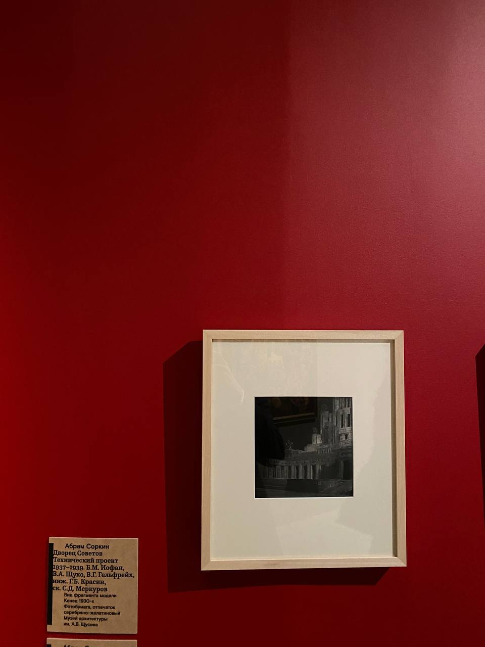 Photo noir et blanc d'un fragment de maquette du Palais des Soviets, dans un cadre clair sur un mur rouge ; à gauche, un cartel au nom d'Abram Sorkine.