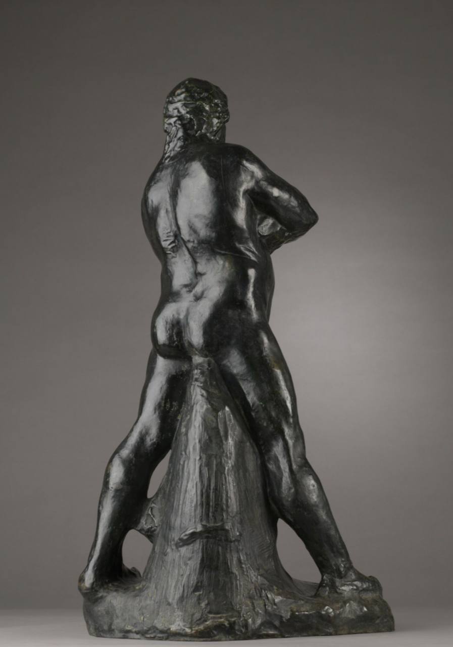 Figure en bronze sombre d'un homme nu vu de dos, jambes écartées, tête tournée, un bras ramené à la taille. Un tronc rugueux se dresse près de lui sur un socle irrégulier.