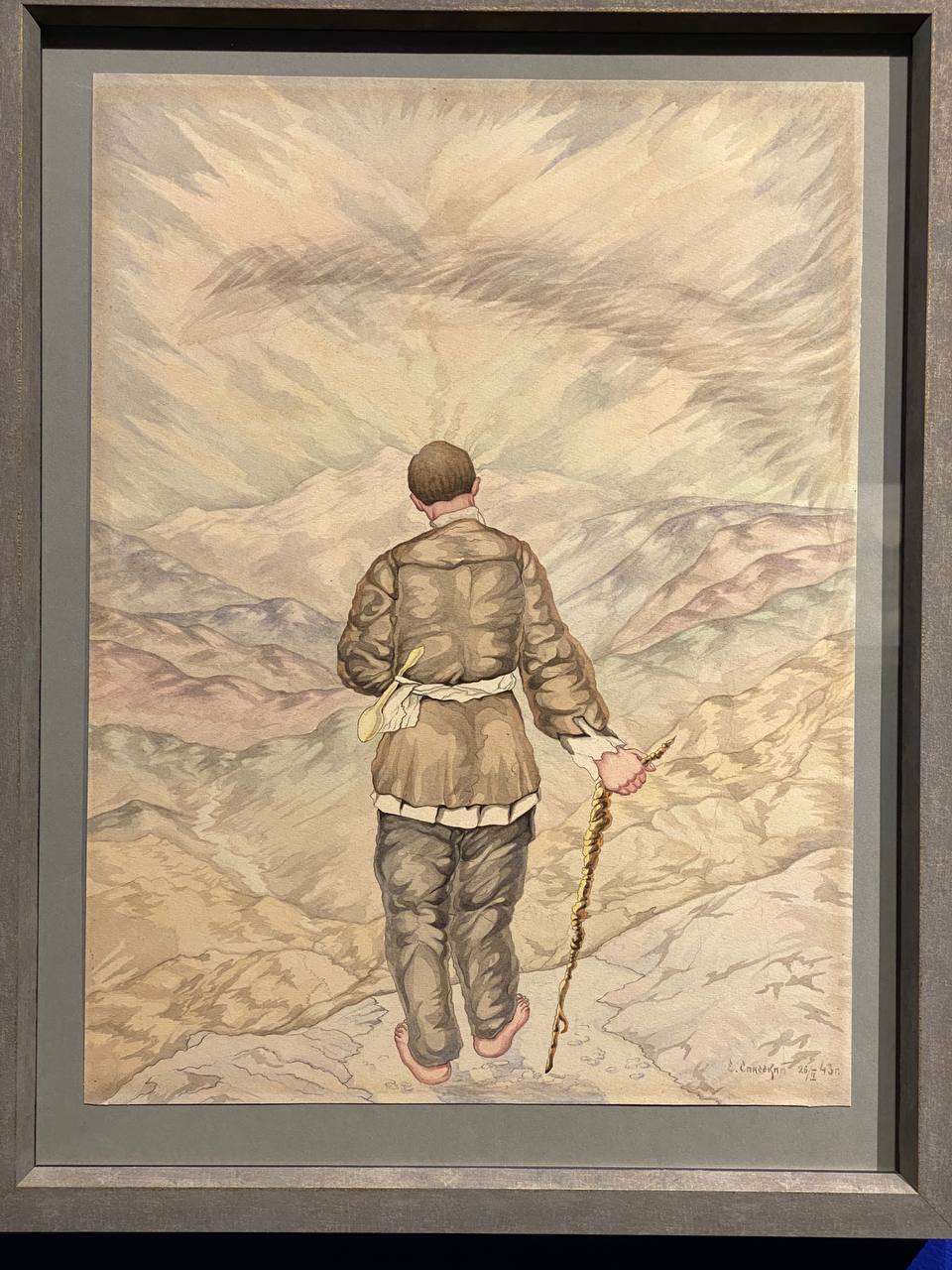 Aquarelle encadrée : un homme pieds nus, en tunique et pantalon, vu de dos, avec un bâton et une cuillère en bois à la ceinture, marche vers des montagnes sous un ciel nuageux.