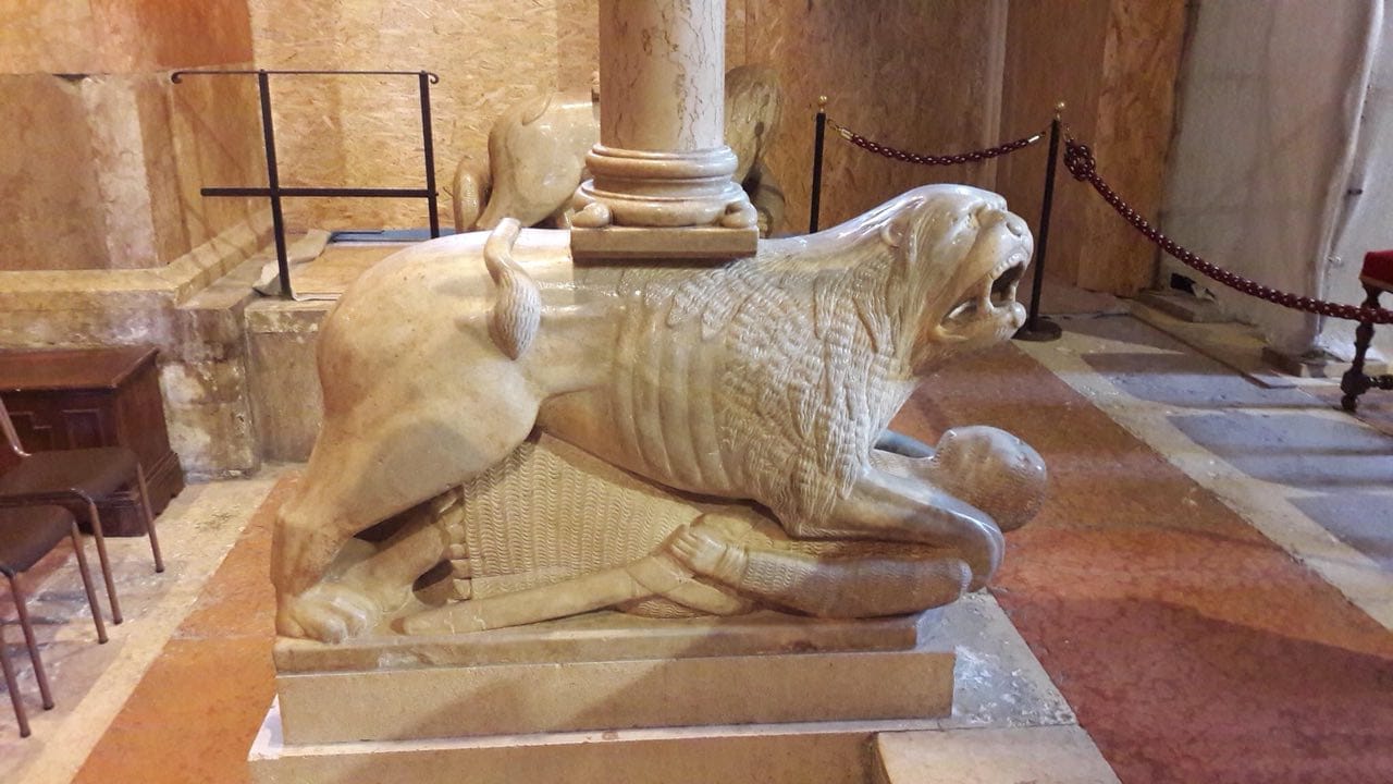 A marble lion with an open mouth stands over a prone knight figure, with a column resting on its back.