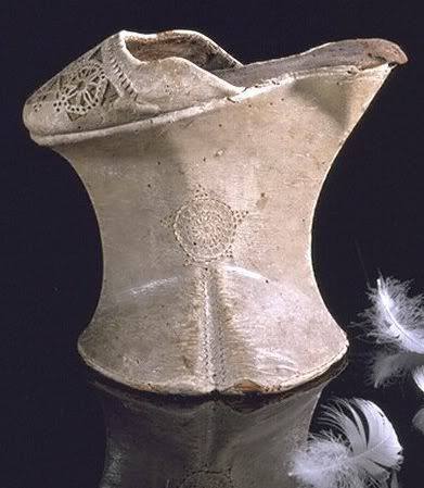 Chaussure en cuir clair sur haute plateforme évasée, ornée de rosaces, sur fond sombre, à côté de plumes blanches.