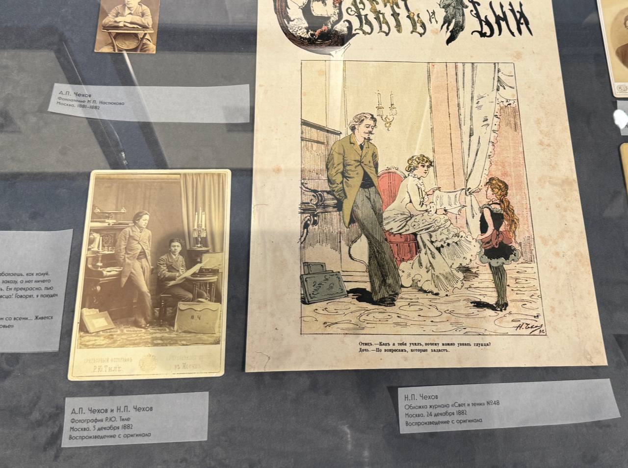 Vitrine de musée : photo cabinet d'A. P. et N. P. Tchekhov dans un intérieur, et couverture en couleur de la revue Svet i teni n° 48 montrant un père, une mère et leur fille.