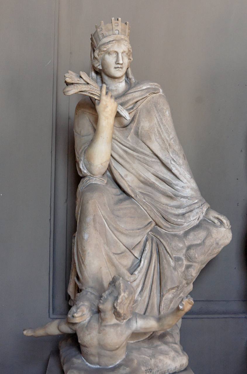 Marble statue of a seated goddess in a crenellated city-wall crown, holding ears of wheat, with a male figure at her feet.