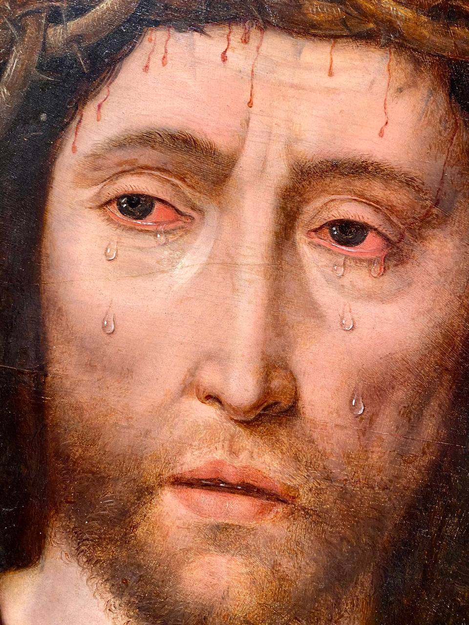 Gros plan sur le visage du Christ couronné d'épines, avec du sang au front et des larmes sur les joues, détail d'une peinture flamande à l'huile.