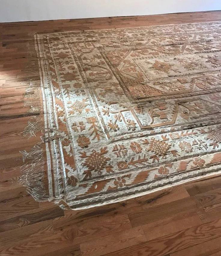 A patterned carpet with fringe carved into the surface of a wooden floor.