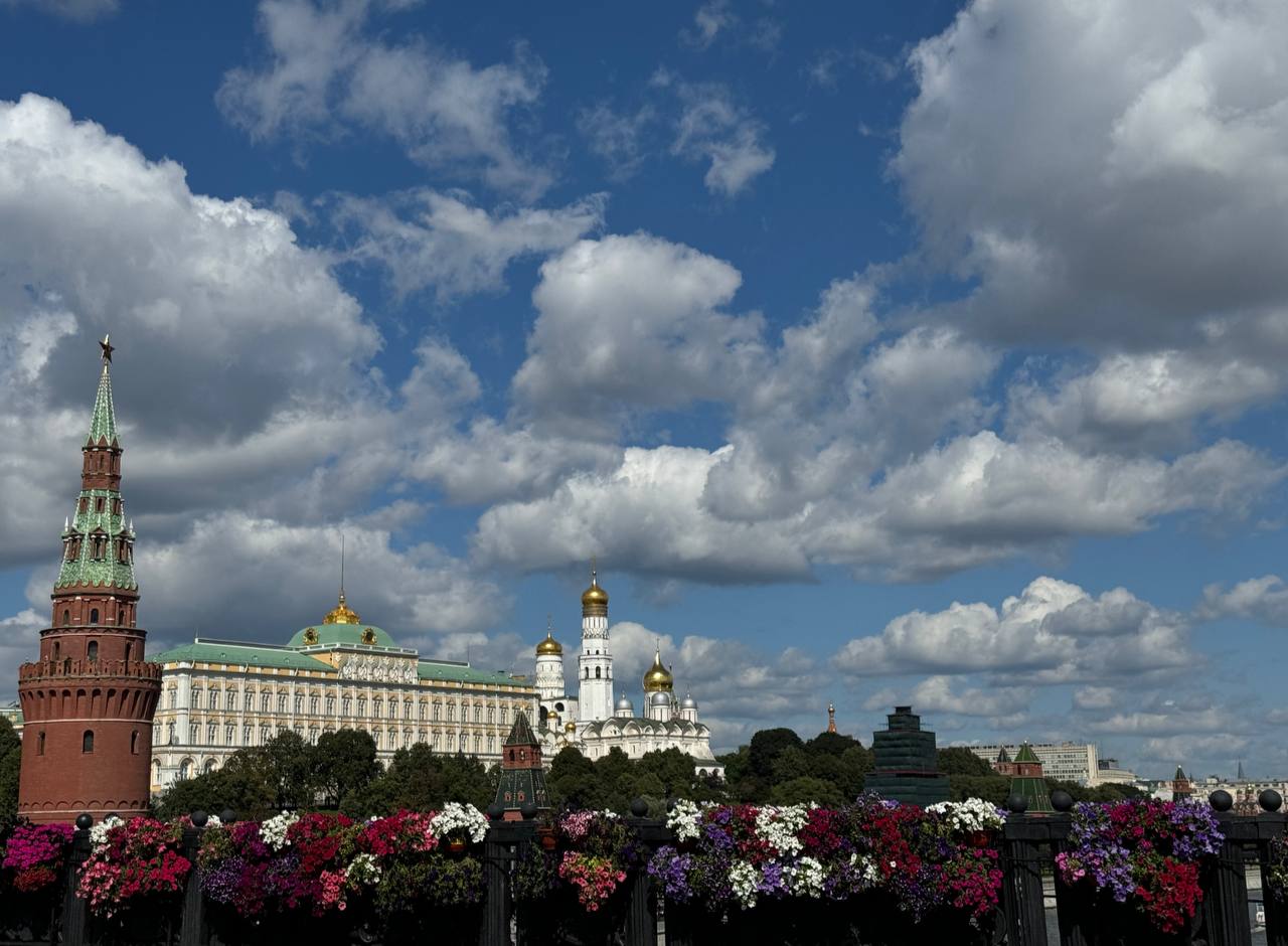 Flowers on the bridge railing, with a Moscow Kremlin tower and palace, the Ivan the Great Bell Tower and a cloudy sky behind.