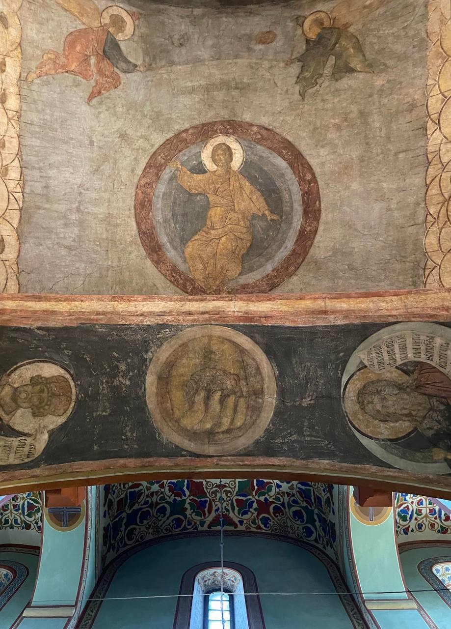 Fresque ancienne d’église : figure nimbée en robe dorée dans un médaillon rond, anges en vol de chaque côté, et en dessous un arc à médaillons et des voûtes ornées.