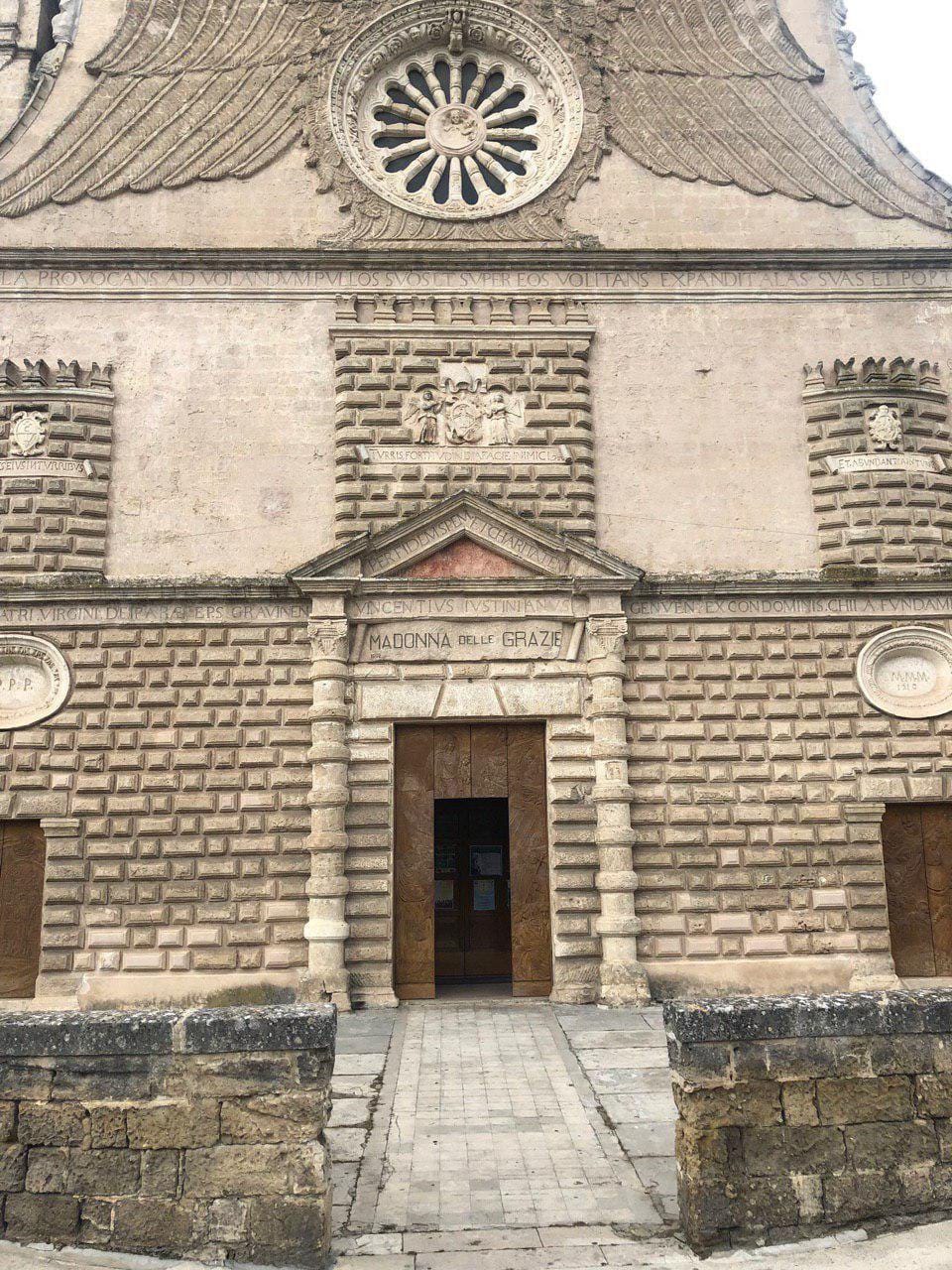 Façade en pierre à bossage, avec rosace, inscriptions latines et portail portant l'inscription Madonna delle Grazie. À l'entrée, des portes en bois sculpté.