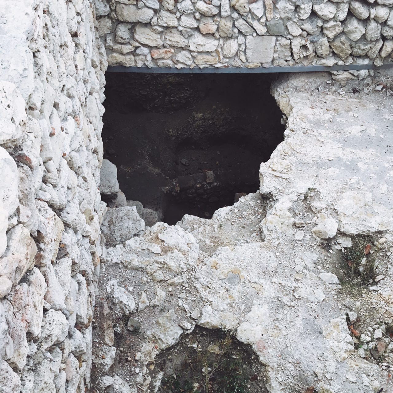 A dark opening in a broken stone surface beside a wall of pale limestone at an excavation site.