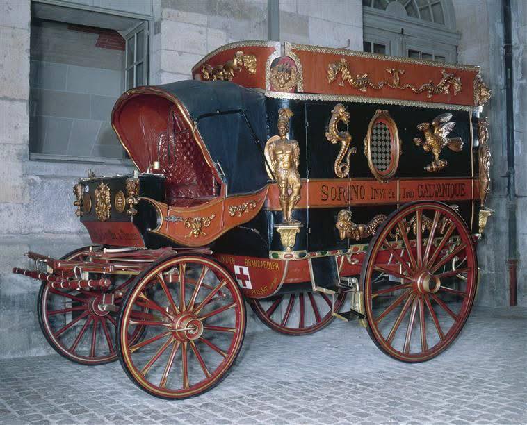 Antique black and red carriage with gilded decoration, the name Sorino on its side and a red cross on the body, in a stone courtyard.