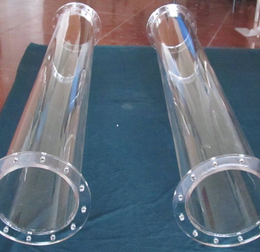 Two long transparent tubes with wide flanges and a ring of holes along the edge lie parallel on dark green cloth. The floor behind is reddish.