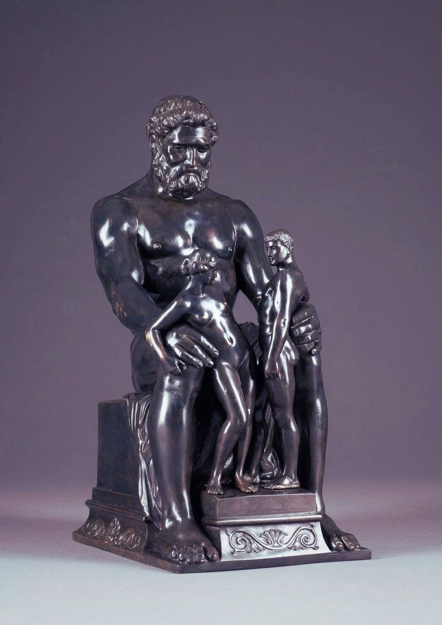 Sculpture en bronze d'un géant barbu et musclé assis, avec deux petites figures nues à ses côtés sur un socle.