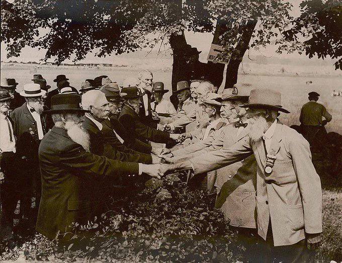 Old photograph of elderly men in hats, many with long beards, shaking hands under a tree.