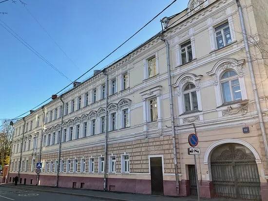 A long pale yellow three-storey building with stucco window surrounds and an arched gateway with wrought-iron doors on the right. Clear blue sky above; a number 10 plate on the wall.