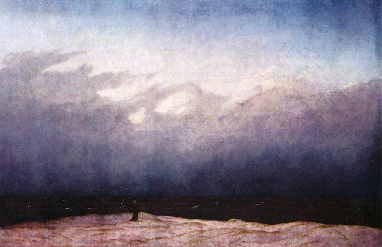 A small dark figure stands on a sandy shore before a dark sea under a vast cloudy sky in Friedrich's painting.