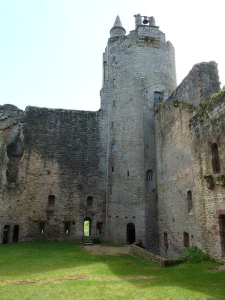Une tour de pierre ronde, surmontée d’une cloche, domine les murs usés d’un château autour d’une cour herbeuse. Fenêtres étroites et portes en arc percent les murs.