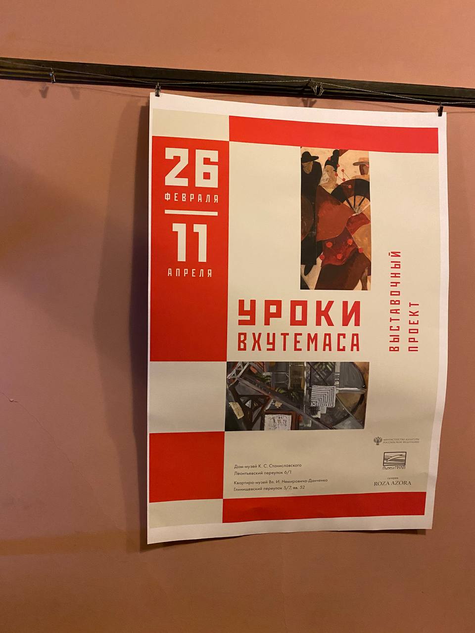 Affiche rouge et blanche accrochée au mur pour l'exposition Leçons du VKhOUTEMAS, avec les dates, deux reproductions de tableaux et les adresses de deux musées.
