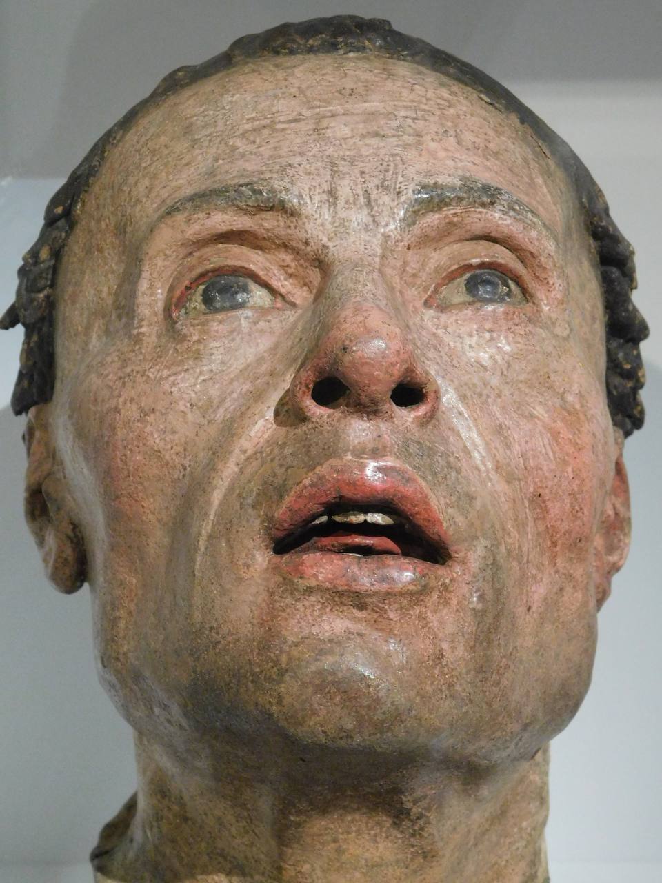 Close-up of a painted terracotta head of a man with parted lips, upturned gaze and short dark hair.