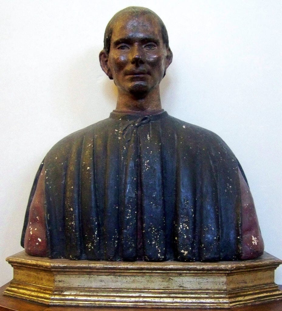 Қара киімді, қызыл жеңді ер адамның өңделген мүсіндік бюсі, жалатылған тұғырда тұр.