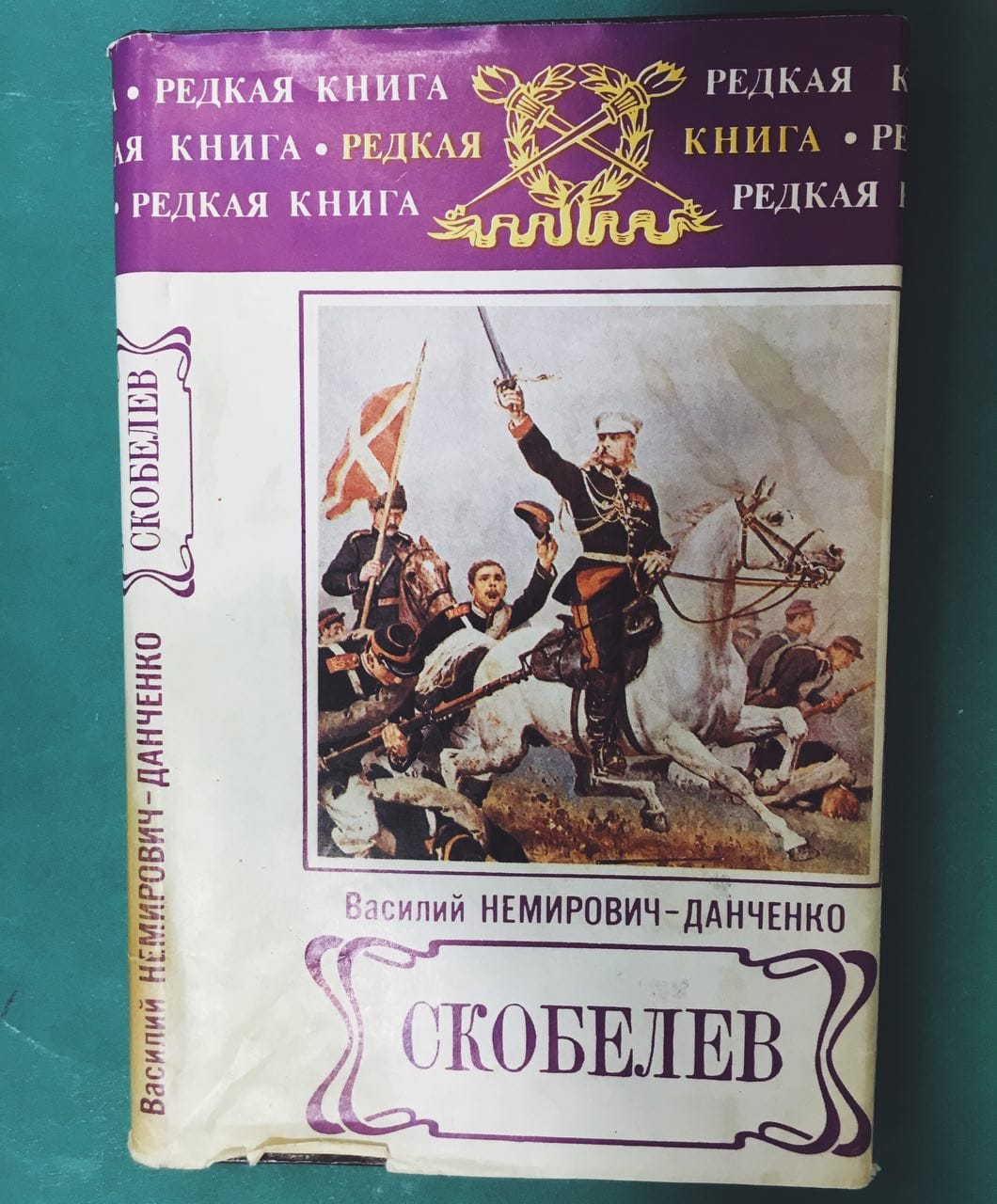 Dust jacket of Vasily Nemirovich-Danchenko's Skobelev: a general on a white horse raising a sword, with soldiers and a banner. A purple Rare Book band runs across the top.