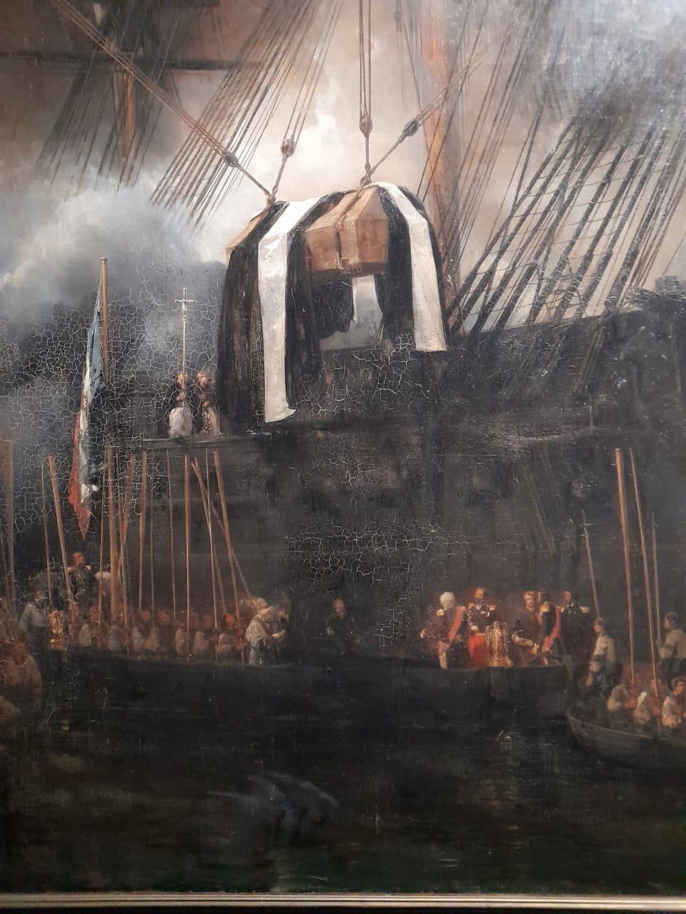 Détail de tableau : un cercueil sous un drap noir et blanc est suspendu aux cordages d'un navire ; en bas, prêtres, officiers et rameurs dans des barques, drapeau à gauche.