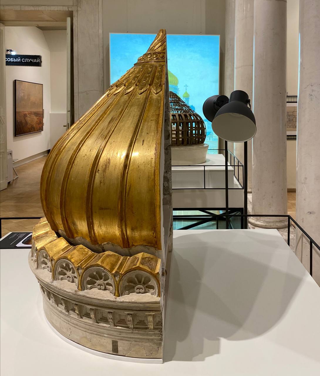 A gilded ribbed onion-shaped dome model on a white plinth in a museum hall.