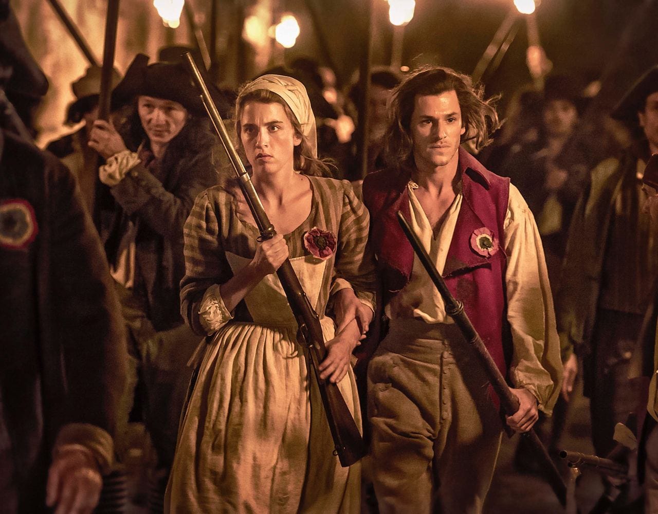Une jeune femme en foulard et un homme en gilet bordeaux marchent bras dessus bras dessous, fusils en main, cocardes au vêtement, suivis d'une foule portant des torches.