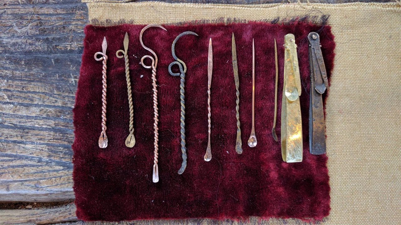 A row of metal manicure tools on red velvet, twisted reconstructions on the left and old originals on the right