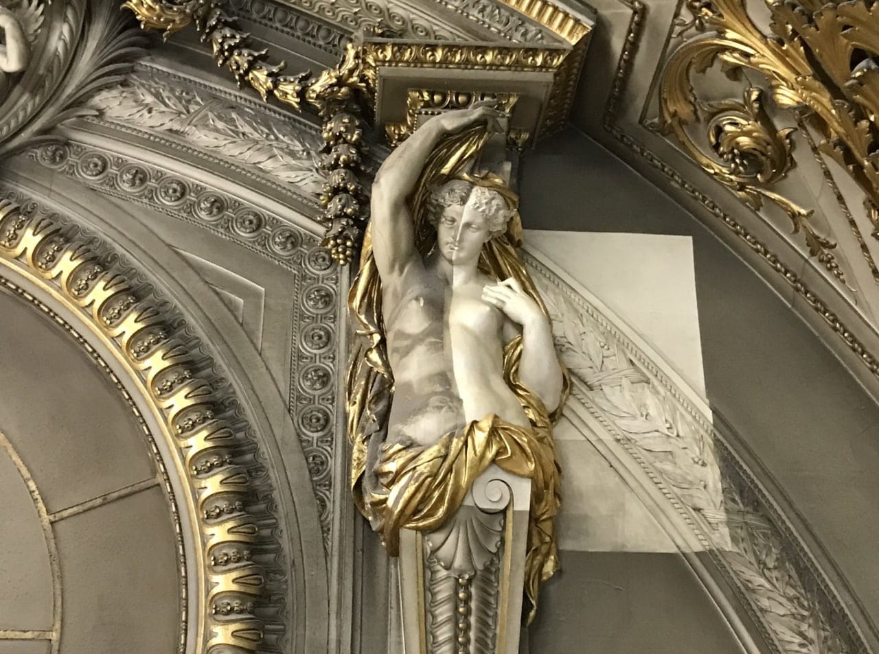 Figure sculptée aux drapés dorés sous une voûte ornée, à moitié nettoyée et à moitié encore couverte d'un voile gris.