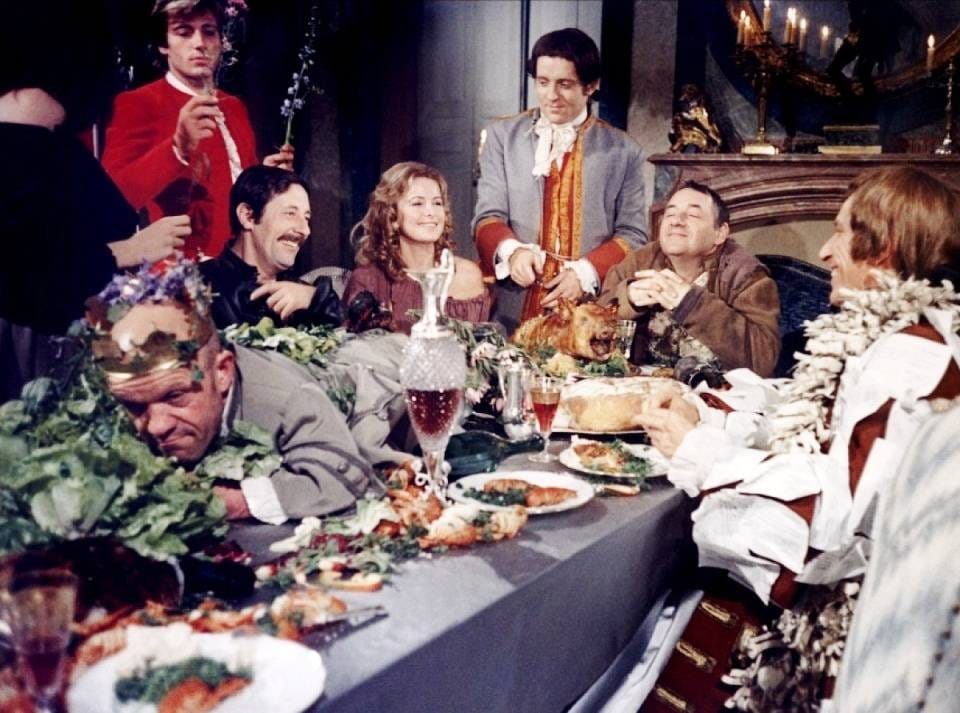 Image du film : des convives en costume du XVIIIe siècle autour d'une table garnie d'un cochon rôti, de verdure et de verres, l'un d'eux affalé face contre la table.