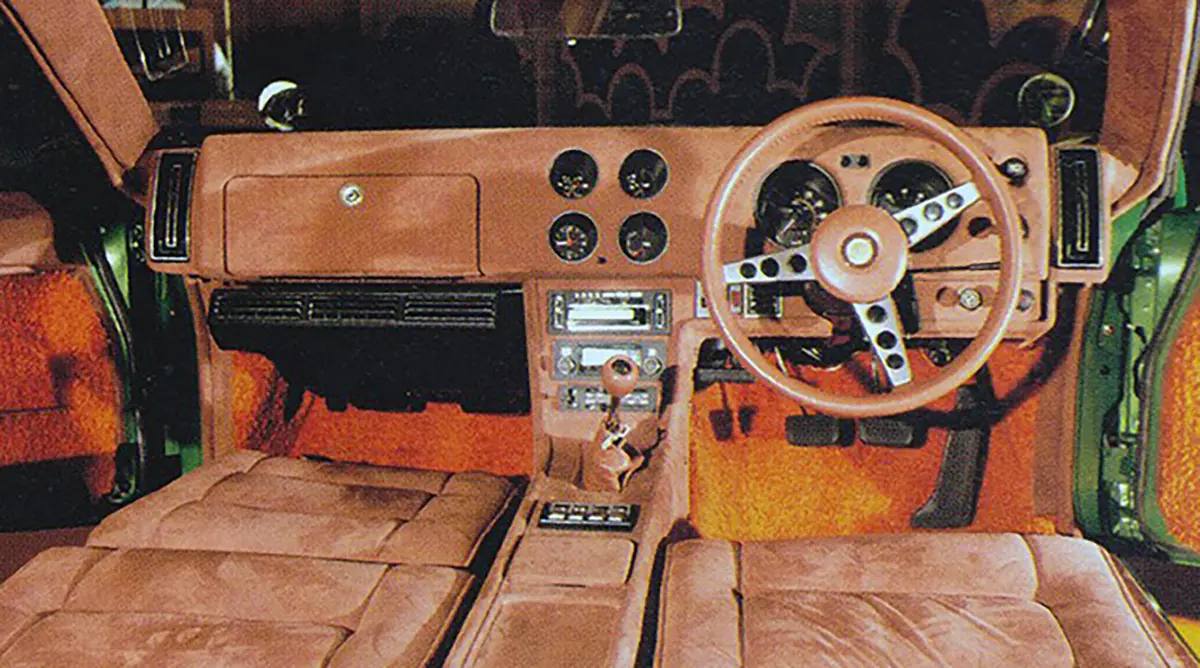 Habitacle avec tableau de bord brun, cadrans ronds, volant à branches à droite, levier de vitesses, autoradio, sièges bruns et moquette orange.
