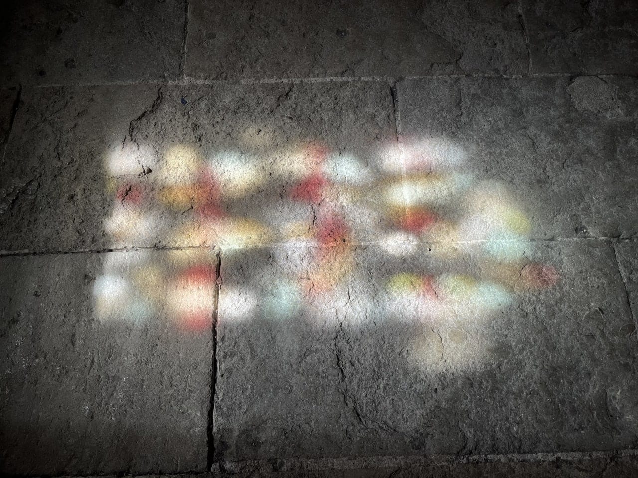 Taches de lumière rouges, jaunes et blanches sur de vieilles dalles de pierre.