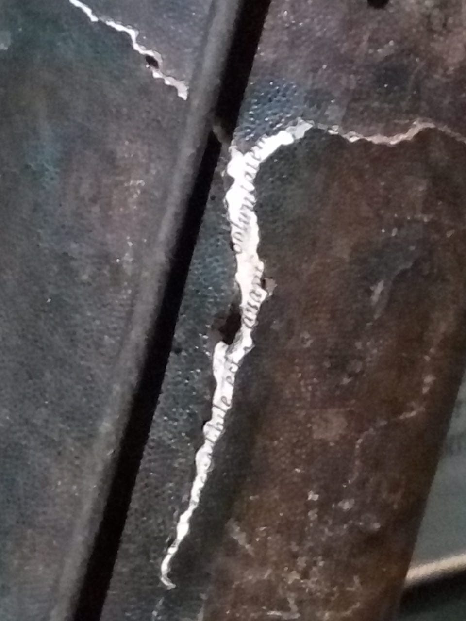Close-up of a dark cracked surface with a white strip of paper showing printed text.