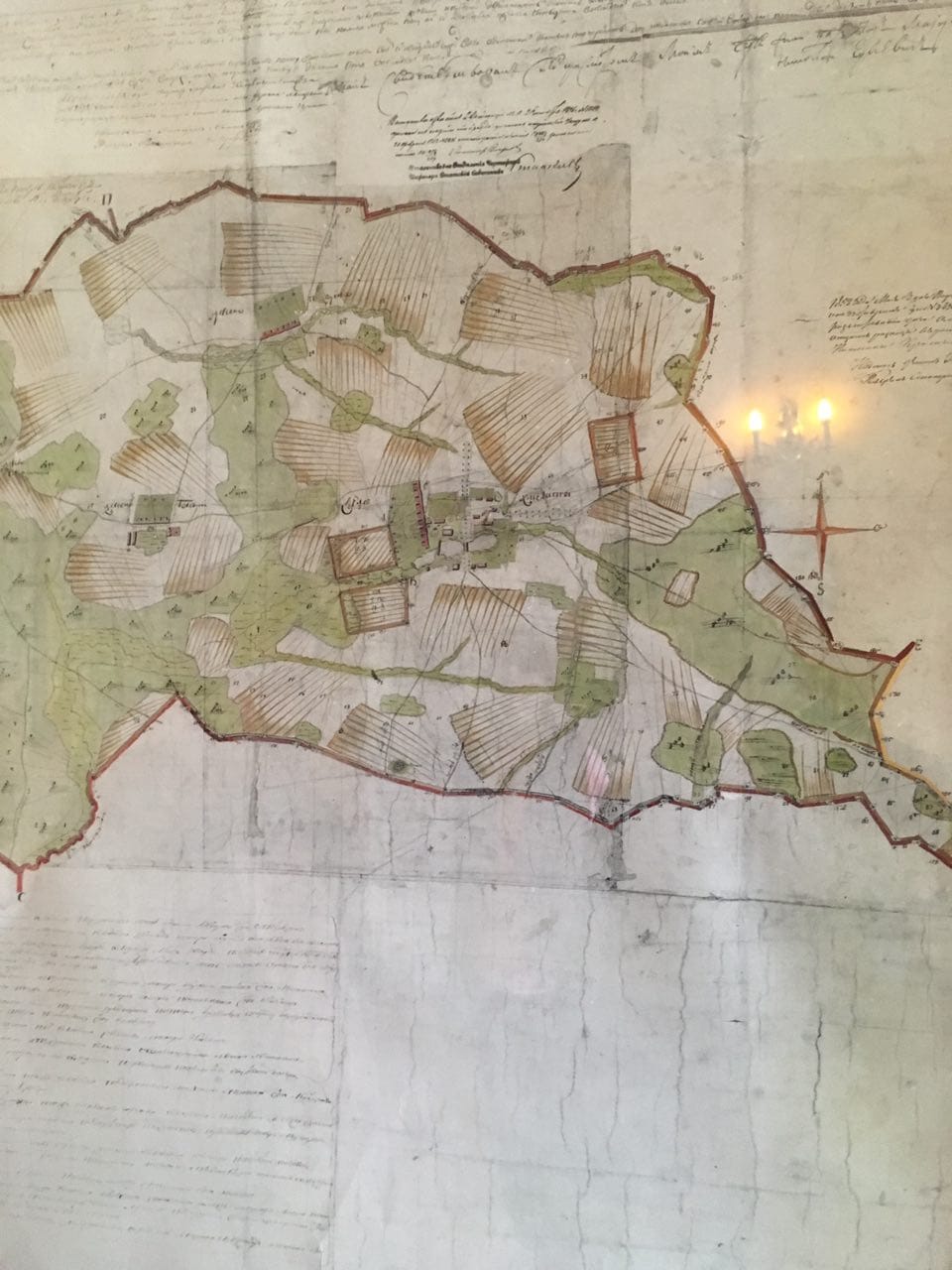 Ancien plan manuscrit d'arpentage des terres de Khmelita avec limites, champs, bois et inscriptions, accroché à un mur.