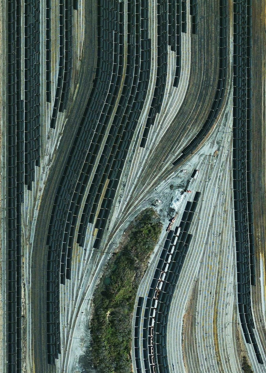 Vue aérienne d'une gare de triage avec de nombreuses voies et de longues rangées courbes de wagons de marchandises sombres.