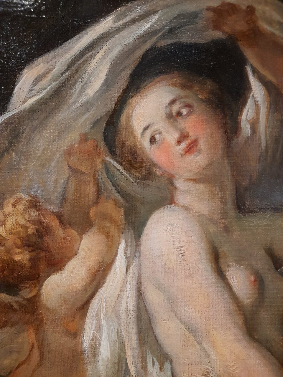Detail of a painting: a young nude woman looks back over her shoulder while infant cupids hold a white veil above her.