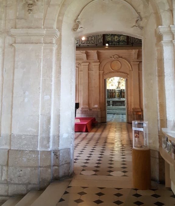 A stone arch and enfilade of rooms with a chequered tiled floor and a red table in the Bishop's Palace in Chartres.