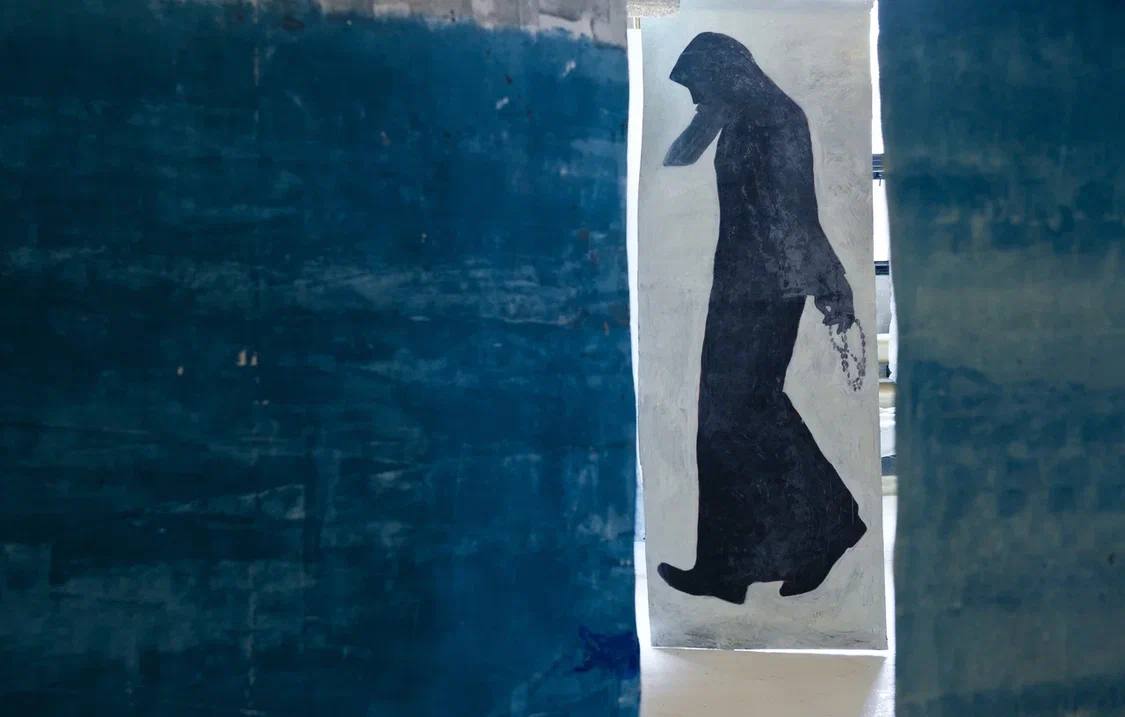 Grande figure noire en long habit à capuche, un chapelet à la main, peinte sur une feuille claire. De part et d'autre, des panneaux d'un bleu profond.