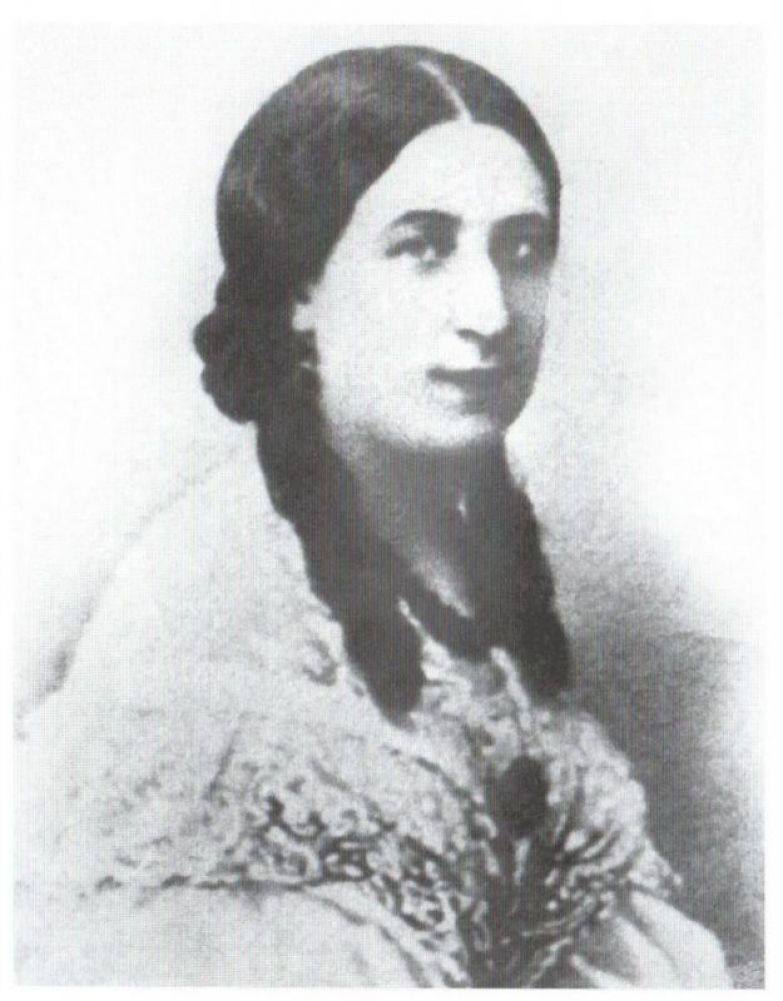 Ancienne photographie en noir et blanc d'une jeune femme aux cheveux bruns séparés par une raie, aux longues tresses sur la poitrine, vêtue de dentelle.