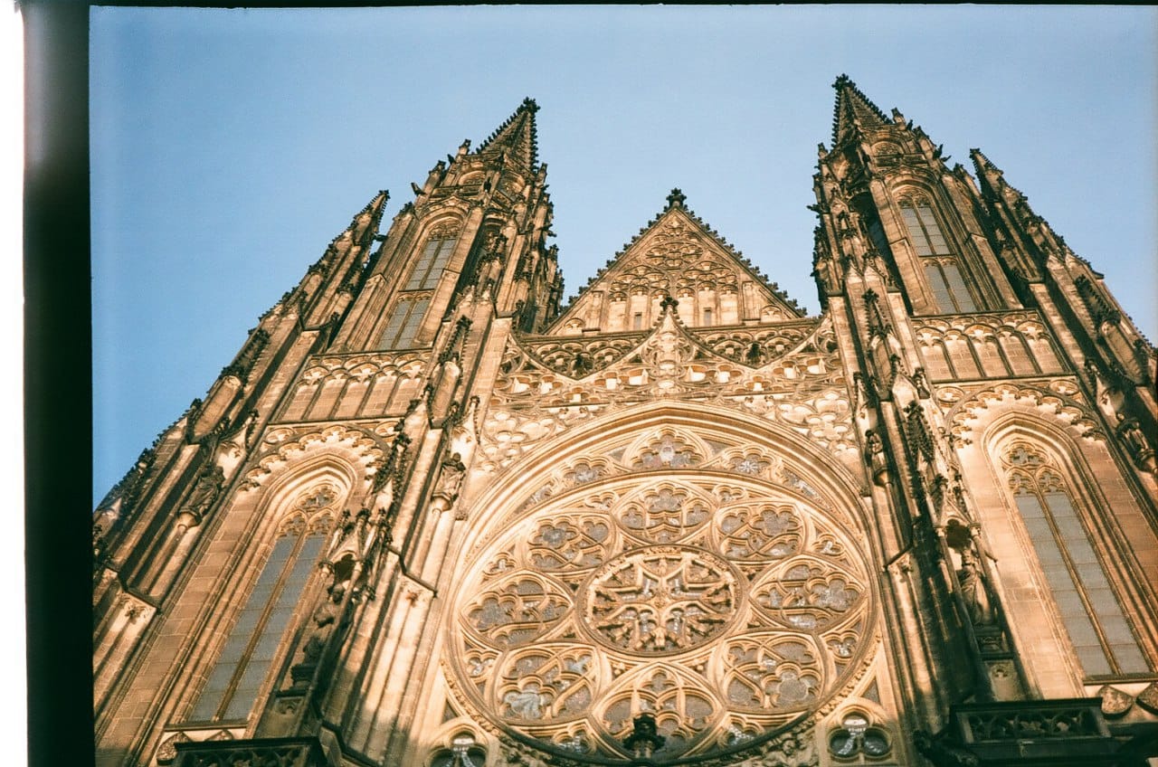 Photographie argentique en contre-plongée des deux flèches et de la grande rosace de la façade gothique d'une cathédrale, sur fond de ciel bleu.