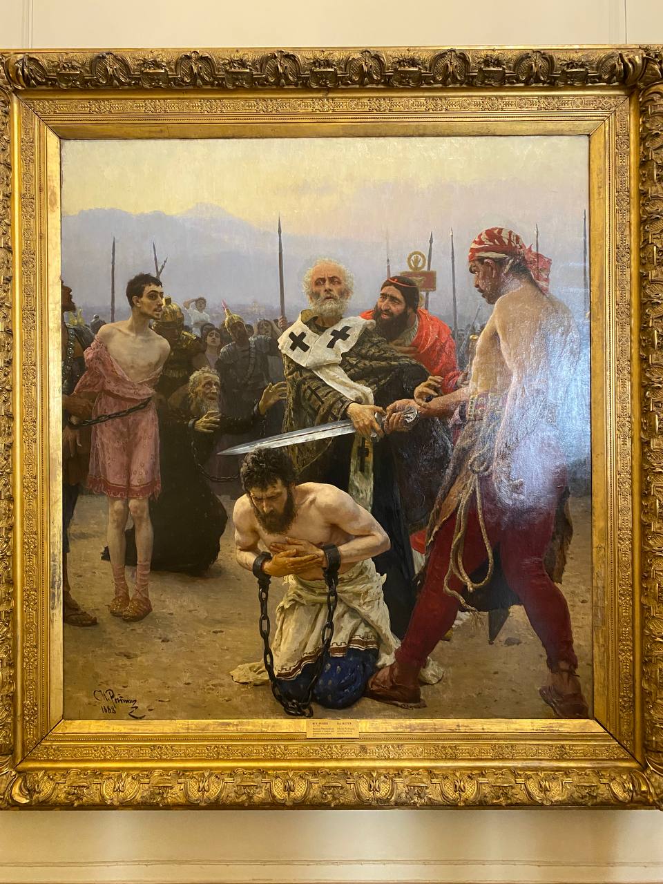 The poet Apollon Maykov prevents the painter Nikolai Kuznetsov from cutting off the head of the writer Ieronim Yasinsky, while the Symbolist Dmitry Merezhkovsky, in chains, contemplates the proceedings with detachment