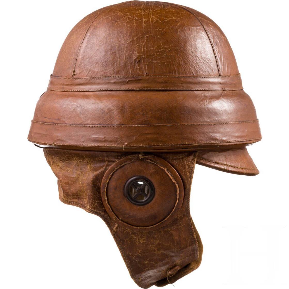 Casque en cuir brun à calotte nervurée, large bandeau, petite visière et cache-oreille à insert métallique. Le cuir est usé et craquelé.