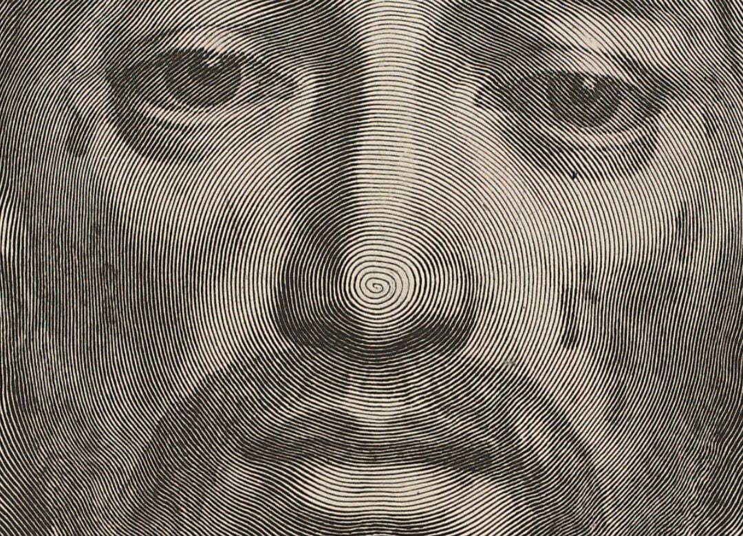 Close detail of an engraving of a face made of concentric lines that spiral outward from the tip of the nose.