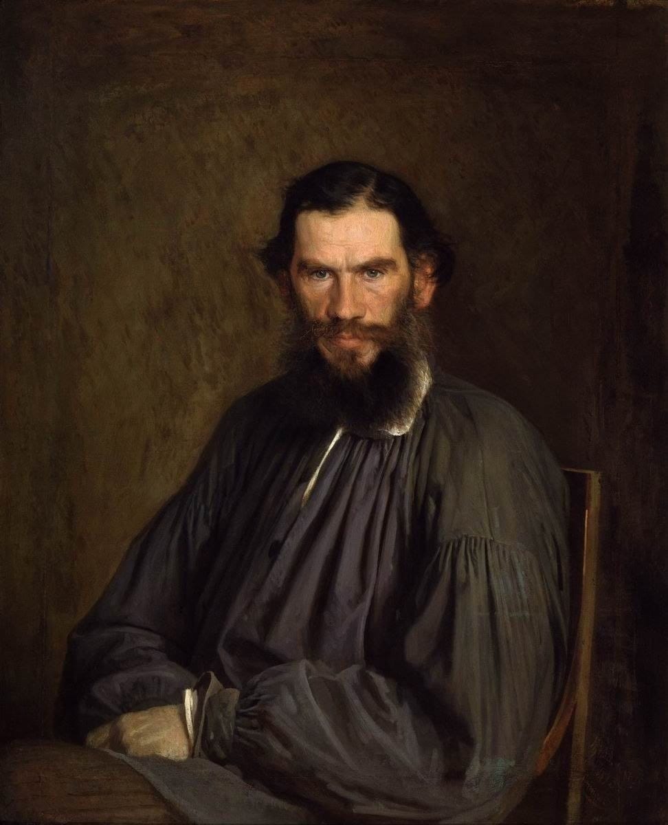 Portrait à l'huile d'un homme brun à la barbe fournie, en ample blouse grise, assis sur une chaise près d'une table, sur fond brun sombre, le regard dirigé vers le spectateur.