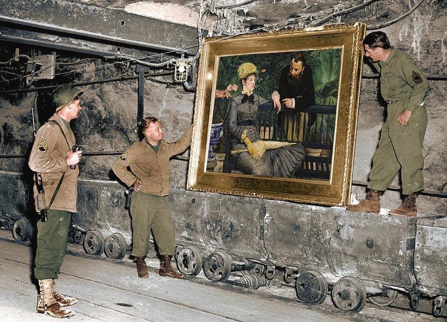 Trois soldats américains dans une galerie de mine souterraine tiennent près d’un wagonnet un tableau de Manet à cadre doré montrant une femme et un homme barbu.