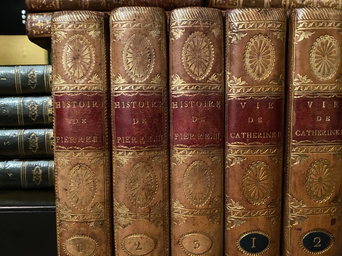 Корешки книг в коричневых кожаных переплётах с золотым тиснением: «Histoire de Pierre III», тома 1–3, и «Vie de Catherine II», тома 1–2.