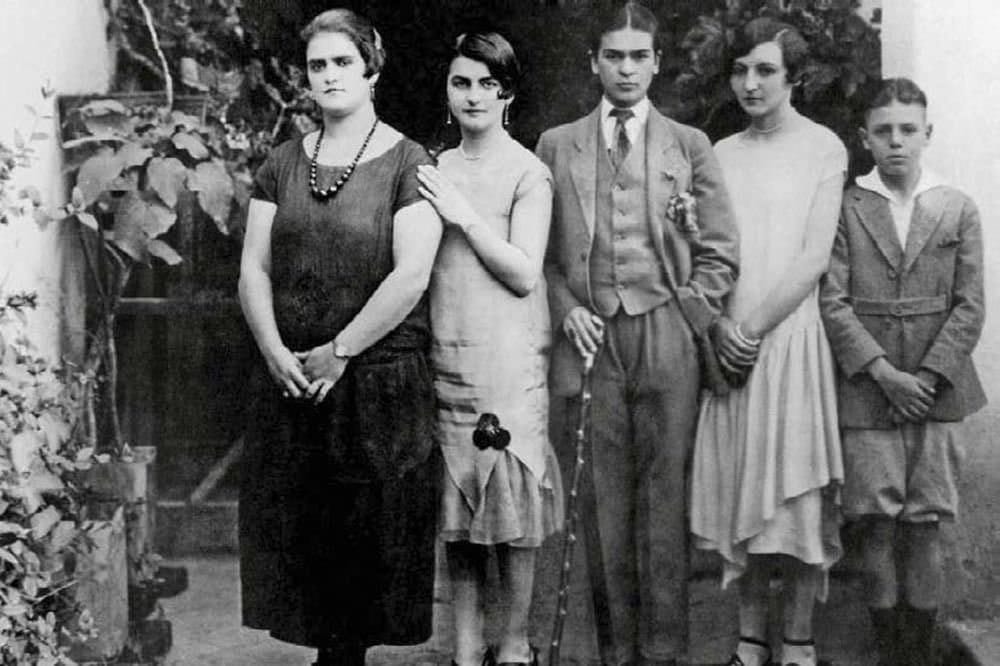 На чёрно-белом снимке в ряд стоят пятеро, в центре человек в костюме с галстуком и тростью, рядом три женщины и мальчик.