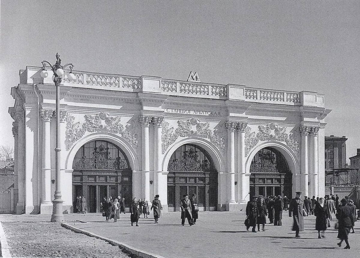 Белый павильон станции Арбатская московского метро с тремя арочными входами и лепным декором, перед ним прохожие, снимок 1953 года.