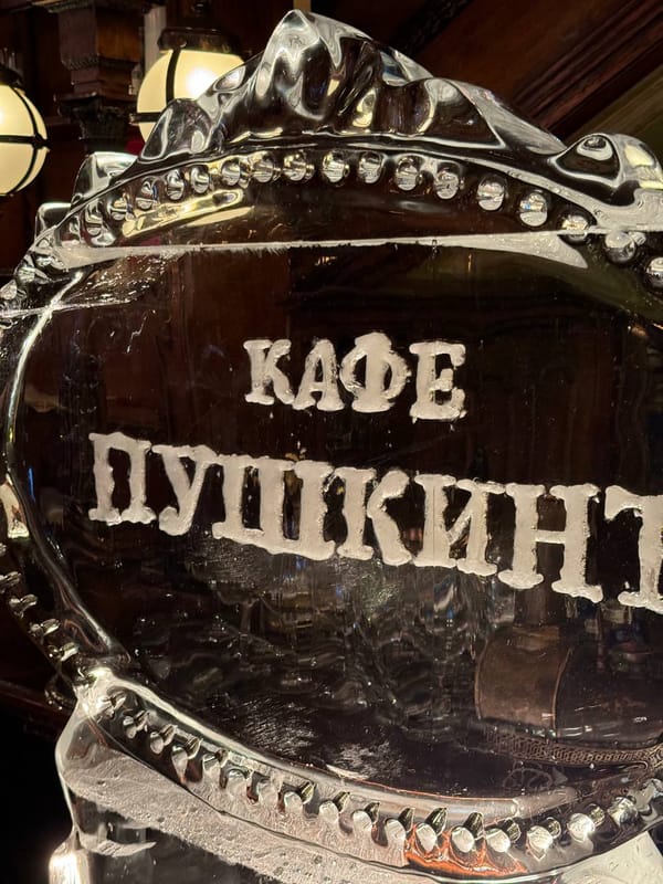 Ледяная скульптура в виде овального медальона с надписью «Кафе Пушкинъ» на фоне тёмных деревянных панелей и ламп.