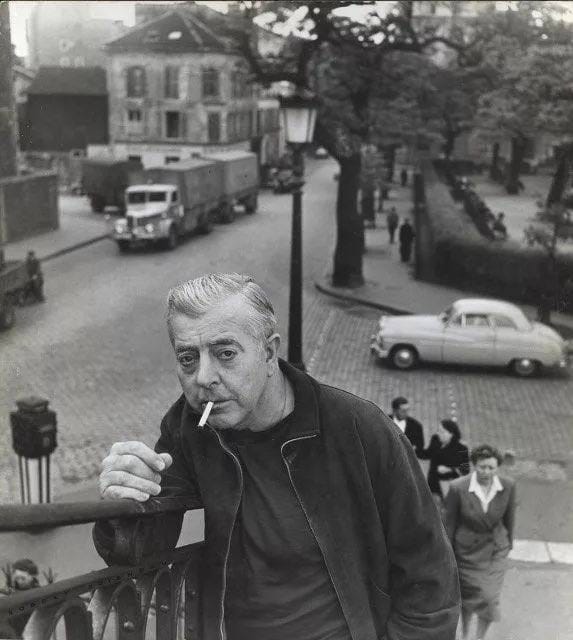 Чёрно-белая фотография седеющего мужчины с сигаретой во рту, который опирается на перила над улицей с грузовиком и легковым автомобилем.
